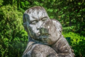A gentle hug of a parent and a child, statue against green leaves