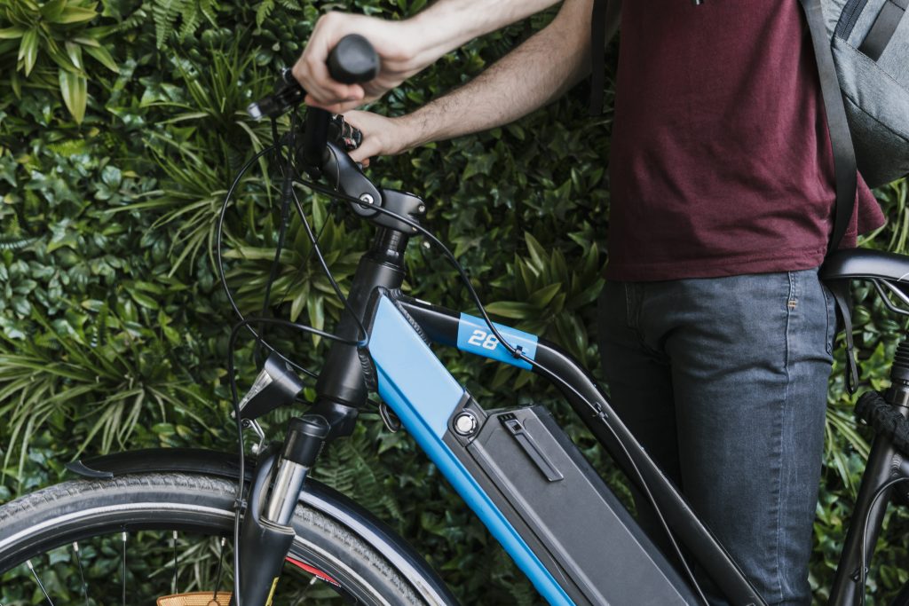 sideways-photo of cyclist-holding-e-bike-with-green planter-wall-background